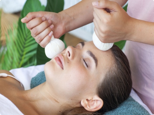 Therapist applying heated herbal compress to release neck and face strain